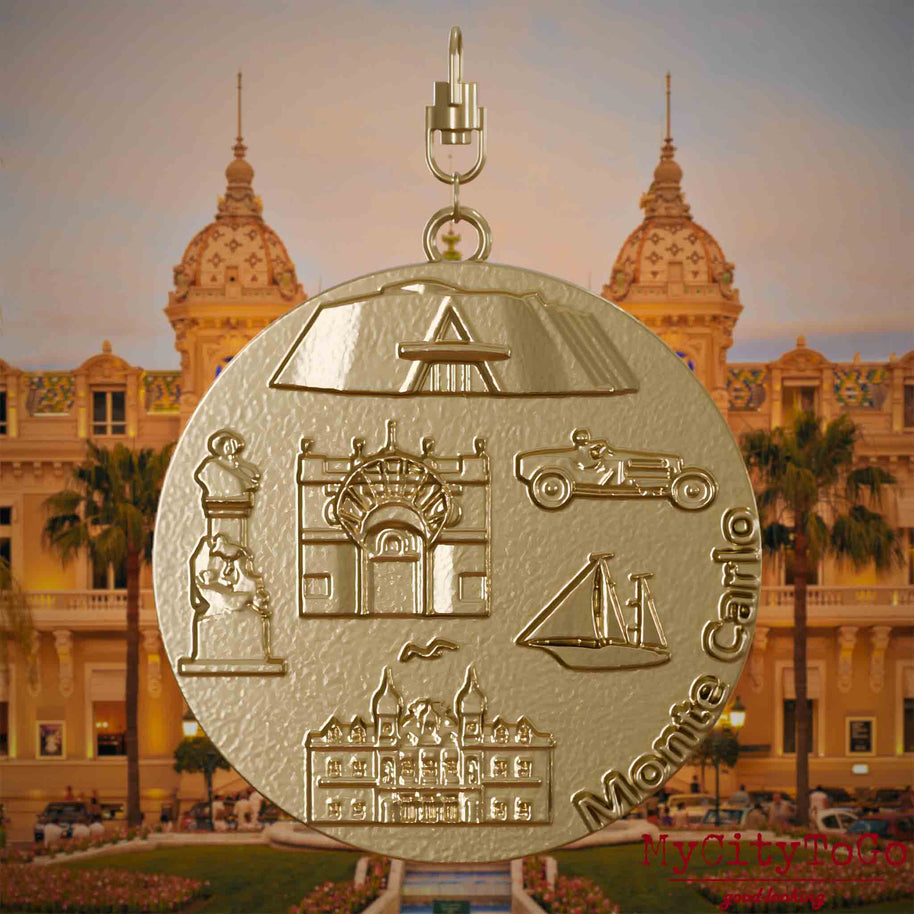 Halskette mit Drehwirbel und Vorderseite eines Schmuckanhängers aus vergoldetem Edelstahl, auf dem Reliefs bekannter Sehenswürdigkeiten der Stadt Monte Carlo abgebildet sind. Den Hintergrund bildet eine Ansicht der Stadt Monte Carlo.
