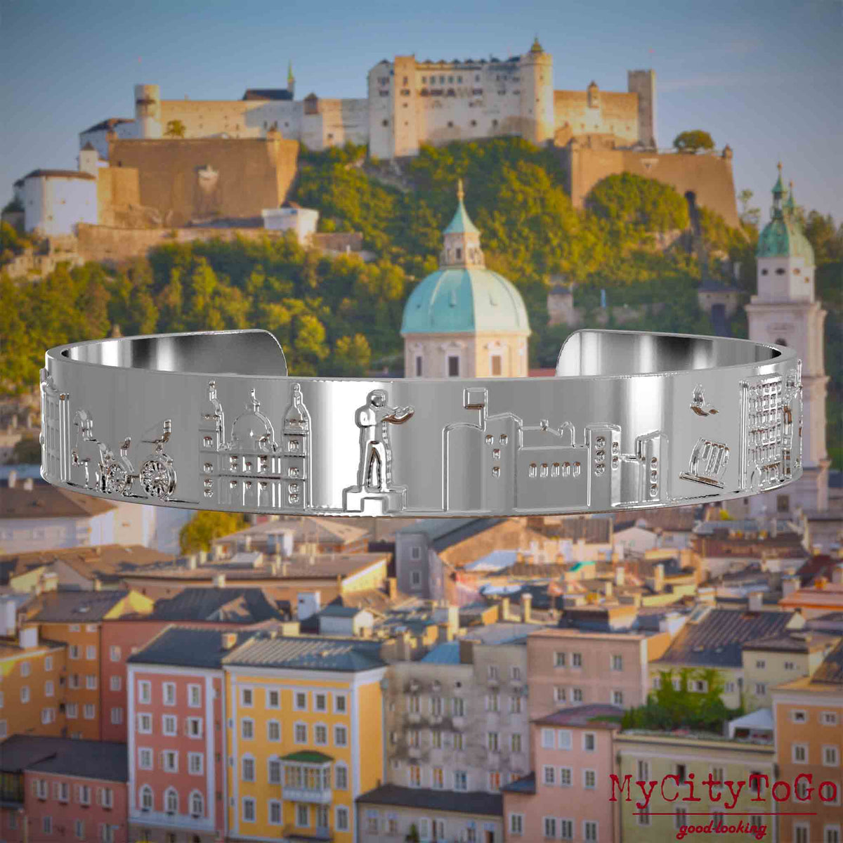 Versilberter Armreif mit Reliefs bekannter Sehenswürdigkeiten der Stadt Salzburg. Den Hintergrund bildet eine Ansicht der Stadt Salzburg.