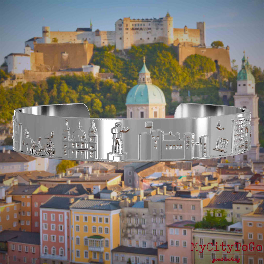 Versilberter Armreif mit Reliefs bekannter Sehenswürdigkeiten der Stadt Salzburg. Den Hintergrund bildet eine Ansicht der Stadt Salzburg.
