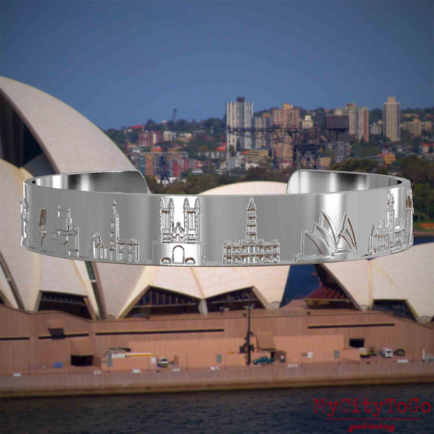 Versilberter Armreif mit Reliefs bekannter Sehenswürdigkeiten der Stadt Sydney. Den Hintergrund bildet eine Ansicht der Stadt Sydney.