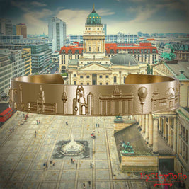 Vergoldeter Armreif aus Edelstahl mit Reliefs bekannter Sehenswürdigkeiten der Stadt Berlin. Den Hintergrund bildet eine Ansicht der Stadt Berlin. 