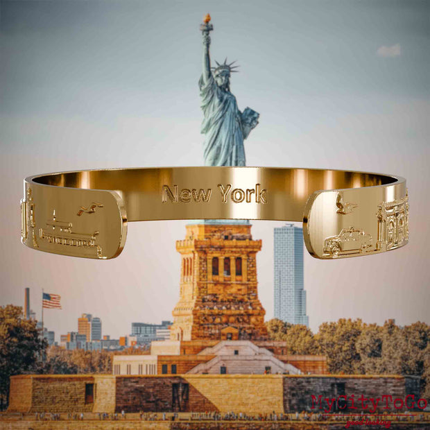 Innenseite eines vergoldeten Armreifs mit Reliefs bekannter Sehenswürdigkeiten der Stadt New York und einer Gravur des Stadtnamens. Den Hintergrund bildet eine Ansicht der Stadt New York.