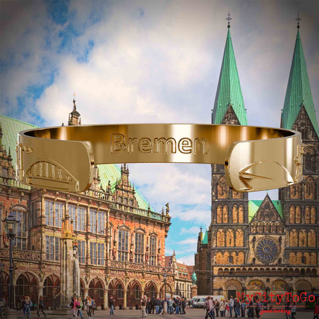 Innenseite eines vergoldeten Armreifs mit Reliefs bekannter Sehenswürdigkeiten der Stadt Bremen und einer Gravur des Stadtnamens. Den Hintergrund bildet eine Ansicht der Stadt Bremen.