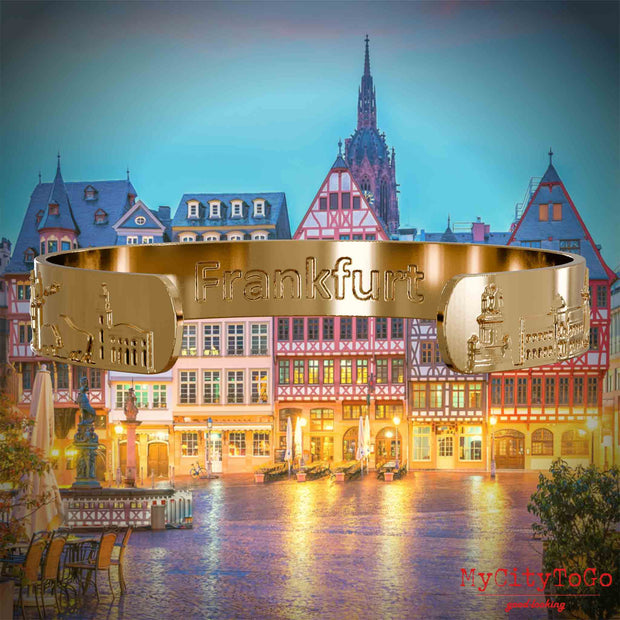 Innenseite eines vergoldeten Armreifs mit Reliefs bekannter Sehenswürdigkeiten der Stadt Frankfurt und einer Gravur des Stadtnamens. Den Hintergrund bildet eine Ansicht der Stadt Frankfurt.