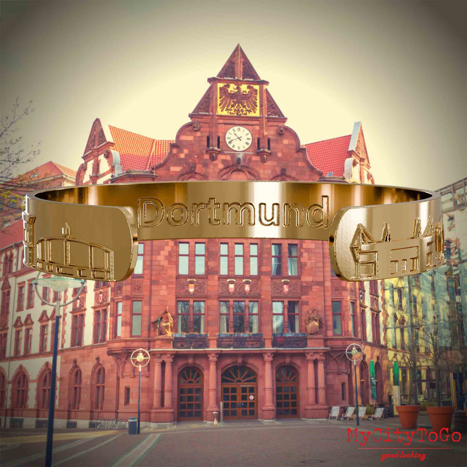 Innenseite eines vergoldeten Armreifs mit Reliefs bekannter Sehenswürdigkeiten der Stadt Dortmund und einer Gravur des Stadtnamens. Den Hintergrund bildet eine Ansicht der Stadt Dortmund.