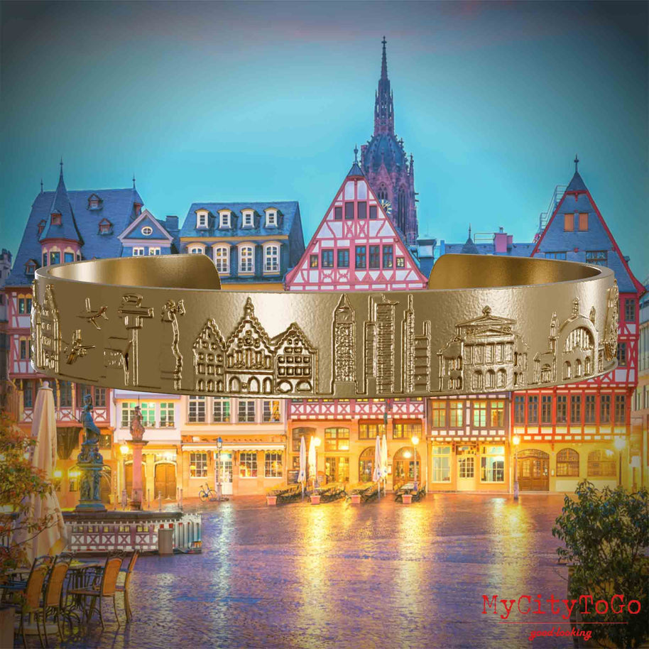 Armreif aus Vergoldetem Edelstahl mit Reliefs bekannter Sehenswürdigkeiten der Stadt Frankfurt. Den Hintergrund bildet eine Ansicht der Stadt Frankfurt.