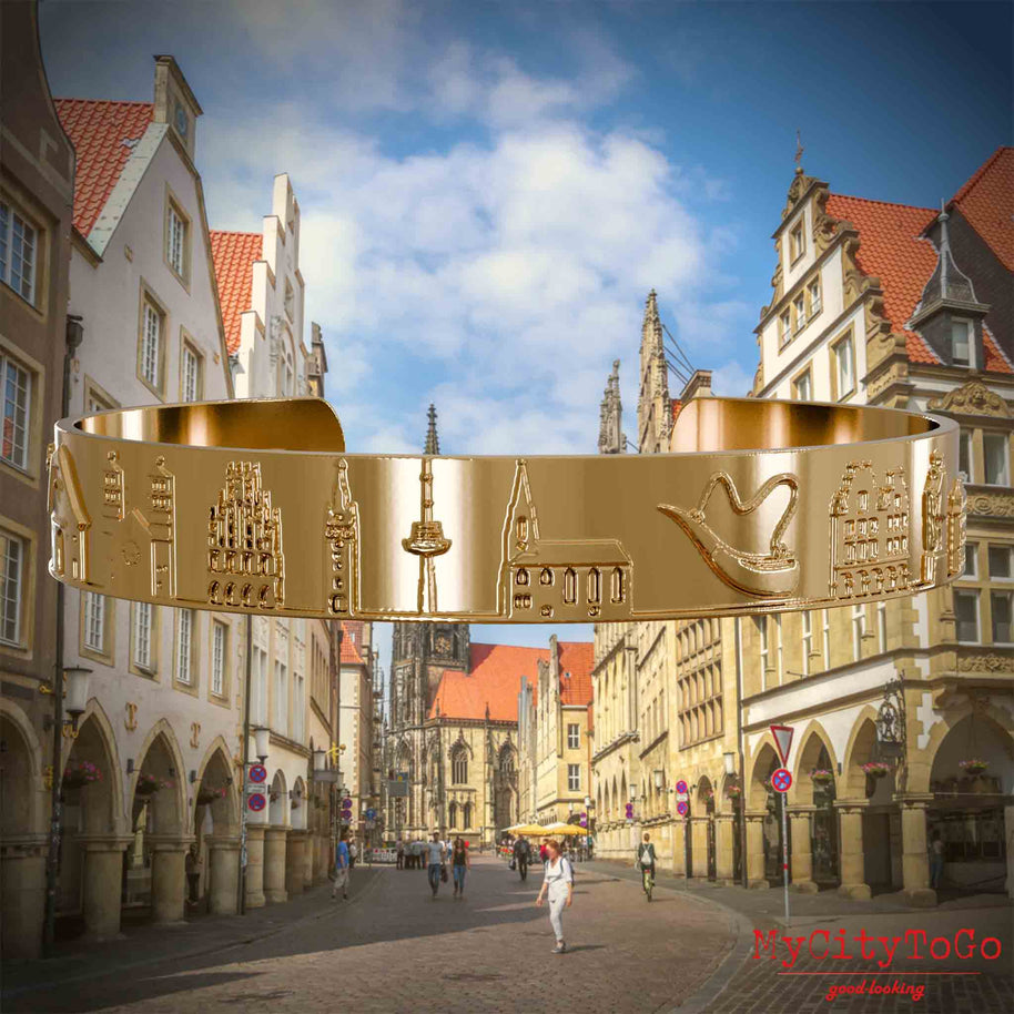 Vergoldeter Armreif mit Reliefs bekannter Sehenswürdigkeiten der Stadt Muenster. Den Hintergrund bildet eine Ansicht der Stadt Muenster.