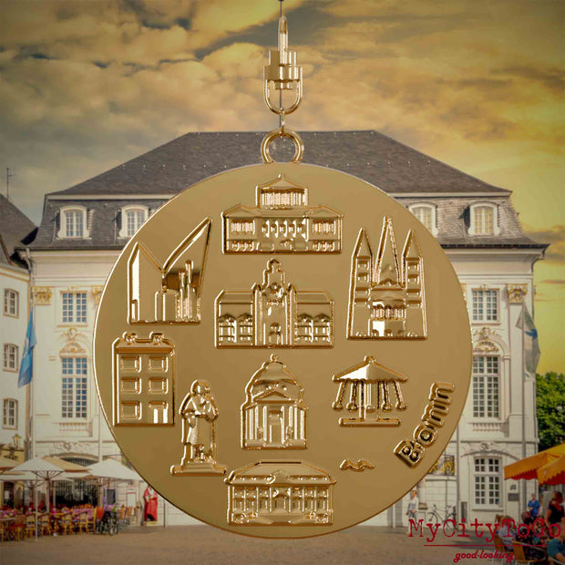 Halskette mit Drehwirbel und Vorderseite eines vergoldeten Schmuckanhängers, auf dem Reliefs bekannter Sehenswürdigkeiten der Stadt Bonn abgebildet sind. Den Hintergrund bildet eine Ansicht der Stadt Bonn.
