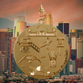 Halskette mit Drehwirbel und Rückseite eines vergoldeten Schmuckanhängers, auf dem Reliefs bekannter Sehenswürdigkeiten der Stadt Los Angeles abgebildet sind. Den Hintergrund bildet eine Ansicht der Stadt Los Angeles.
