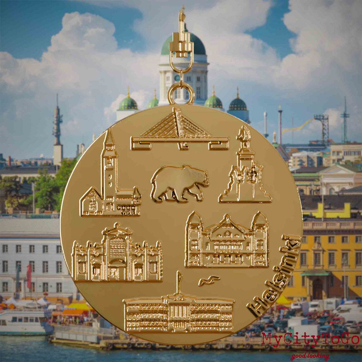 Halskette mit Drehwirbel und Rückseite eines vergoldeten Schmuckanhängers, auf dem Reliefs bekannter Sehenswürdigkeiten der Stadt Helsinki abgebildet sind. Den Hintergrund bildet eine Ansicht der Stadt Helsinki.

