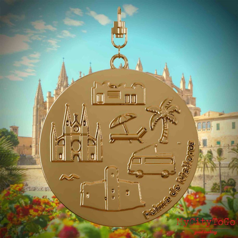 Halskette mit Drehwirbel und Rückseite eines vergoldeten Schmuckanhängers, auf dem Reliefs bekannter Sehenswürdigkeiten der Stadt Palma de Mallorca abgebildet sind. Den Hintergrund bildet eine Ansicht der Stadt Palma de Mallorca.
