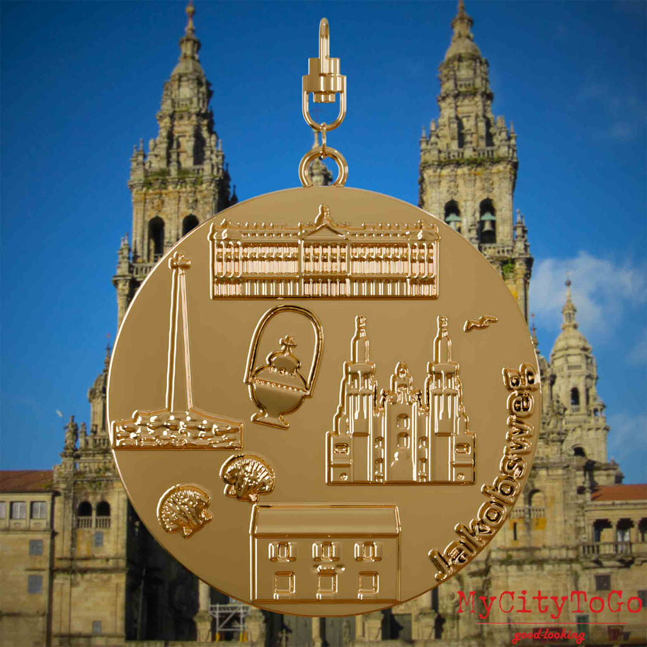 Halskette mit Drehwirbel und Rückseite eines vergoldeten Schmuckanhängers, auf dem Reliefs bekannter Sehenswürdigkeiten des Jakobwegs abgebildet sind. Den Hintergrund bildet eine Ansicht der Stadt Santiago de Compostela.
