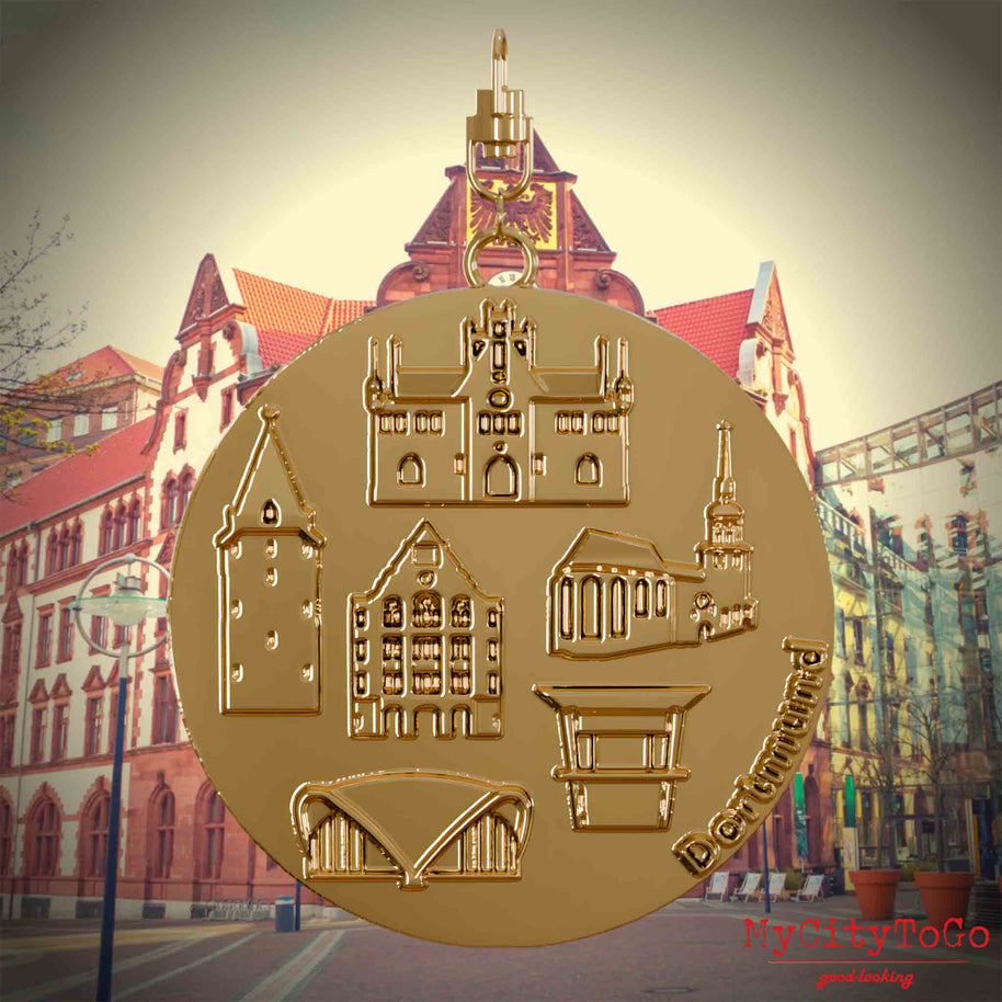 Halskette mit Drehwirbel und Rückseite eines vergoldeten Schmuckanhängers, auf dem Reliefs bekannter Sehenswürdigkeiten der Stadt Dortmund abgebildet sind. Den Hintergrund bildet eine Ansicht der Stadt Dortmund.