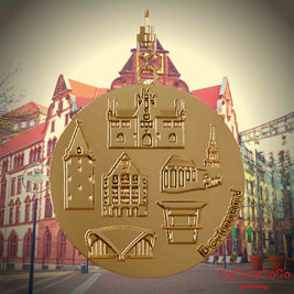 Halskette mit Drehwirbel und Rückseite eines vergoldeten Schmuckanhängers, auf dem Reliefs bekannter Sehenswürdigkeiten der Stadt Dortmund abgebildet sind. Den Hintergrund bildet eine Ansicht der Stadt Dortmund.