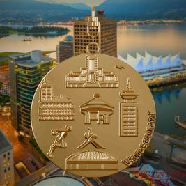 Halskette mit Drehwirbel und Rückseite eines vergoldeten Schmuckanhängers, auf dem Reliefs bekannter Sehenswürdigkeiten der Stadt Vancouver abgebildet sind. Den Hintergrund bildet eine Ansicht der Stadt Vancouver.
