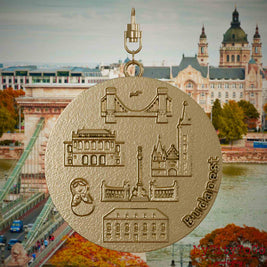 Halskette mit Drehwirbel und Vorderseite eines Schmuckanhängers aus vergoldetem Edelstahl, auf dem Reliefs bekannter Sehenswürdigkeiten der Stadt Budapest abgebildet sind. Den Hintergrund bildet eine Ansicht der Stadt Budapest.
