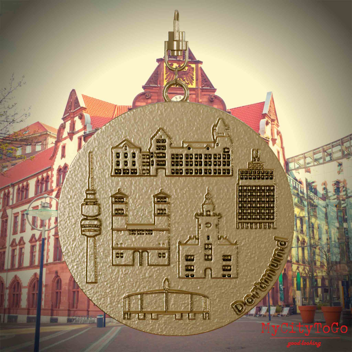 Halskette mit Drehwirbel und Vorderseite eines Schmuckanhängers aus vergoldetem Edelstahl, auf dem Reliefs bekannter Sehenswürdigkeiten der Stadt Dortmund abgebildet sind. Den Hintergrund bildet eine Ansicht der Stadt Dortmund.