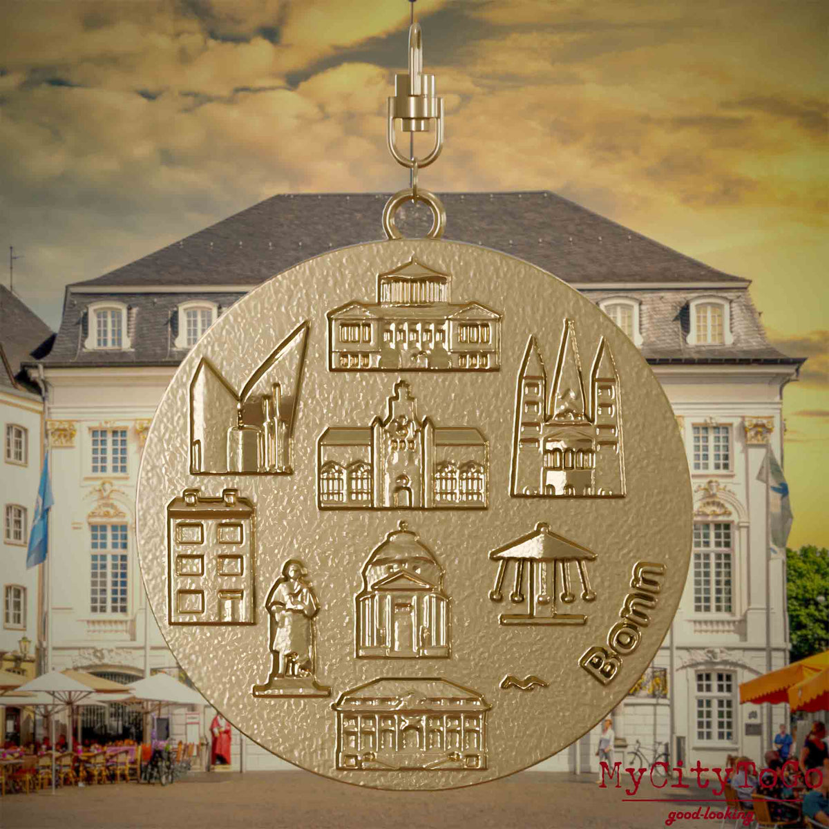 Halskette mit Drehwirbel und Vorderseite eines Schmuckanhängers aus vergoldetem Edelstahl, auf dem Reliefs bekannter Sehenswürdigkeiten der Stadt Bonn abgebildet sind. Den Hintergrund bildet eine Ansicht der Stadt Bonn.
