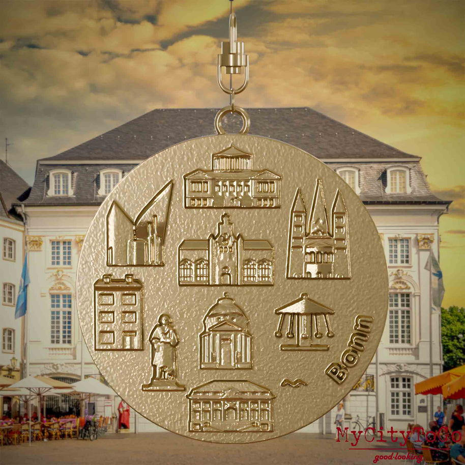 Halskette mit Drehwirbel und Vorderseite eines Schmuckanhängers aus vergoldetem Edelstahl, auf dem Reliefs bekannter Sehenswürdigkeiten der Stadt Bonn abgebildet sind. Den Hintergrund bildet eine Ansicht der Stadt Bonn.
