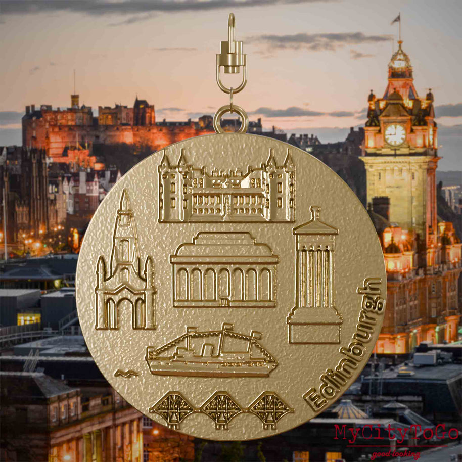 Halskette mit Drehwirbel und Rückseite eines Schmuckanhängers aus vergoldetem Edelstahl, auf dem Reliefs bekannter Sehenswürdigkeiten der Stadt Edinburgh abgebildet sind. Den Hintergrund bildet eine Ansicht der Stadt Edinburgh.
