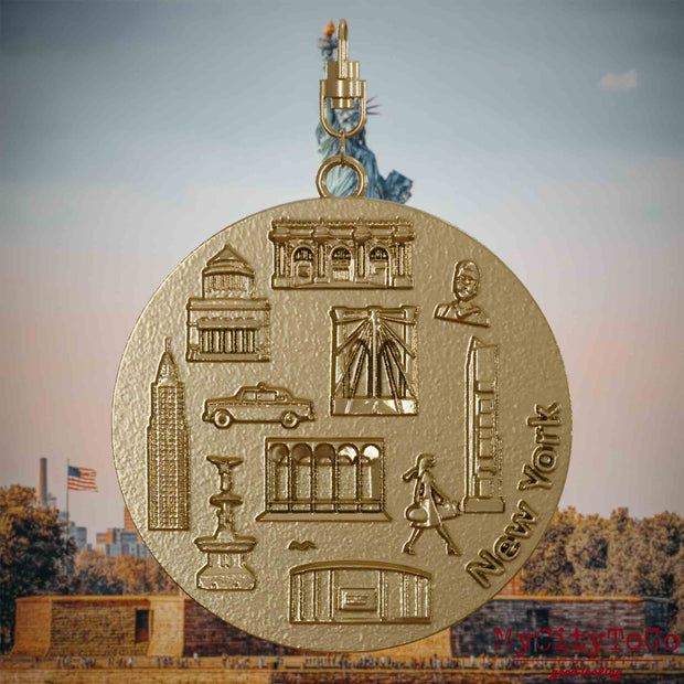 Halskette mit Drehwirbel und Rückseite eines Schmuckanhängers aus vergoldetem Edelstahl, auf dem Reliefs bekannter Sehenswürdigkeiten der Stadt New York abgebildet sind. Den Hintergrund bildet eine Ansicht der Stadt New York.
