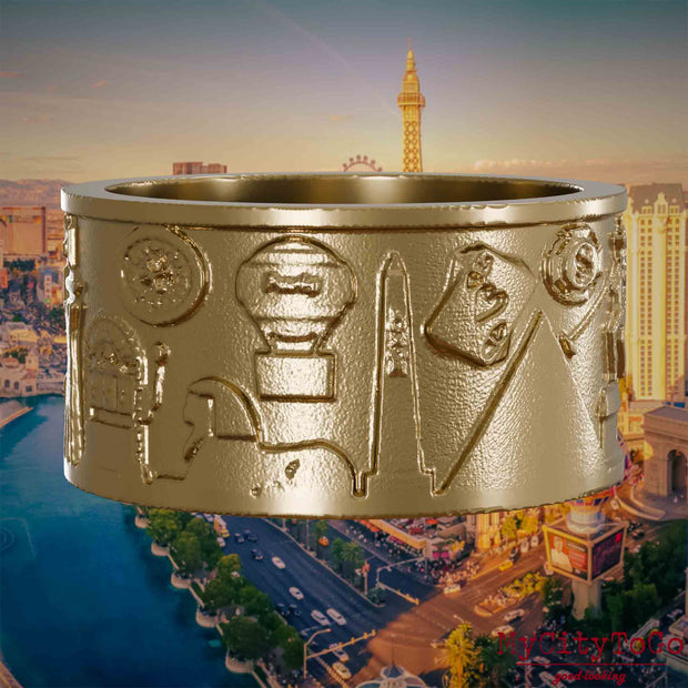 Ring aus vergoldetem Edelstahl mit Reliefs bekannter Sehenswürdigkeiten der Stadt Las Vegas. Den Hintergrund bildet eine Ansicht der Stadt Las Vegas.