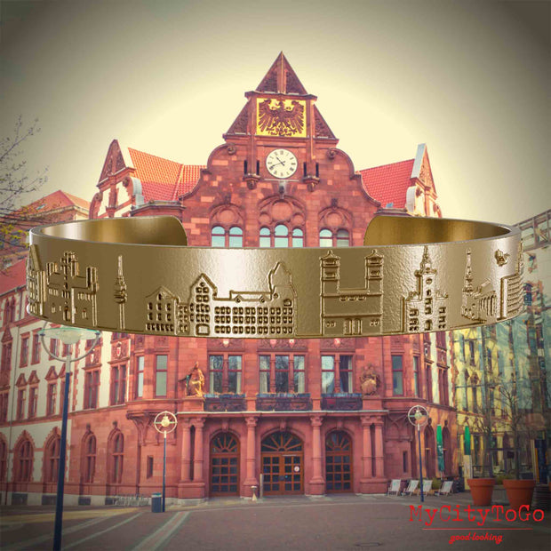 Armreif aus vergoldetem Edelstahl mit Reliefs bekannter Sehenswürdigkeiten der Stadt Dortmund. Den Hintergrund bildet eine Ansicht der Stadt Dortmund.