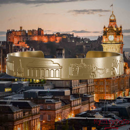 Armreif aus vergoldetem Edelstahl mit Reliefs bekannter Sehenswürdigkeiten der Stadt Edinburgh. Den Hintergrund bildet eine Ansicht der Stadt Edinburgh.
