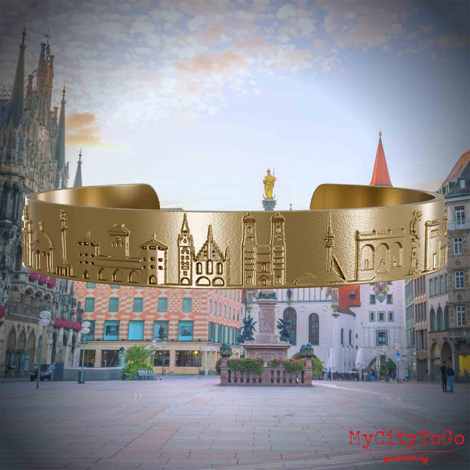 Armreif aus vergoldetem Edelstahl mit Reliefs bekannter Sehenswürdigkeiten der Stadt München. Den Hintergrund bildet eine Ansicht der Stadt Muenchen.