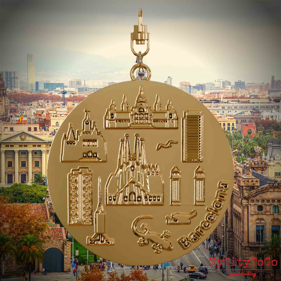 Halskette mit Drehwirbel und Rückseite eines vergoldeten Schmuckanhängers, auf dem Reliefs bekannter Sehenswürdigkeiten der Stadt Barcelona abgebildet sind. Den Hintergrund bildet eine Ansicht der Stadt Barcelona.
