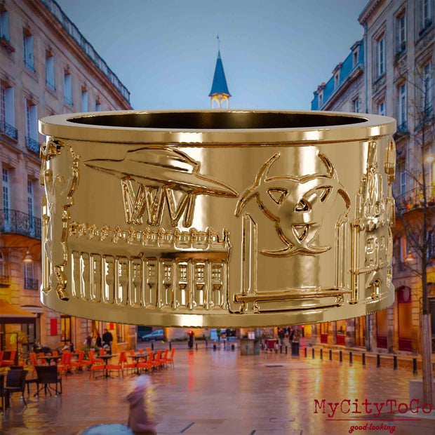 Vergoldeter Ring mit Reliefs bekannter Sehenswürdigkeiten der Stadt Bordeaux. Den Hintergrund bildet eine Ansicht der Stadt Bordeaux.