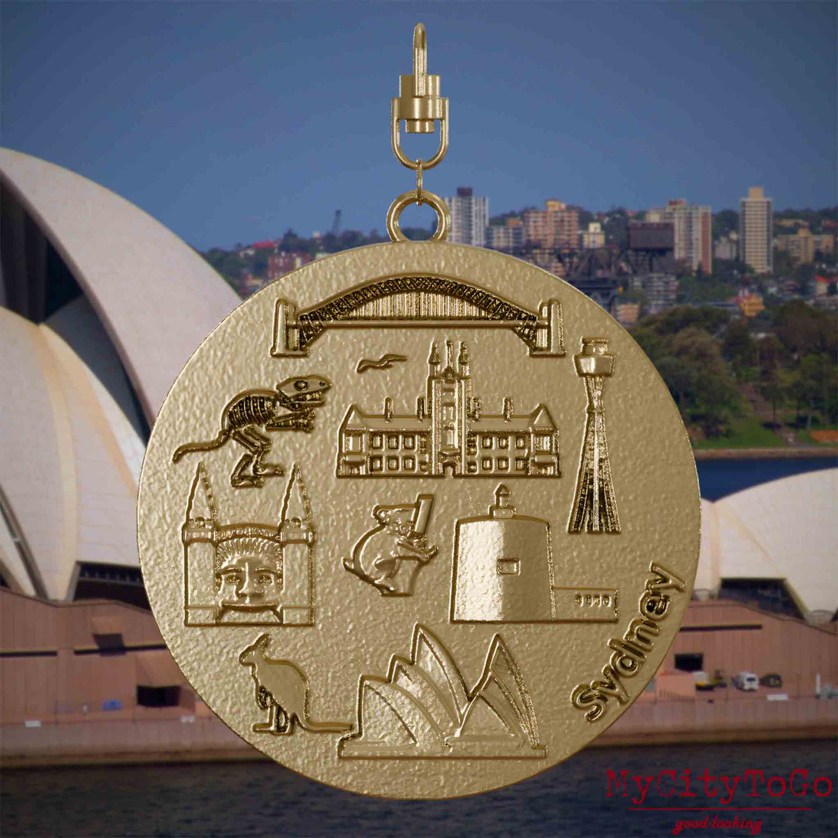 Halskette mit Drehwirbel und Vorderseite eines Schmuckanhängers aus vergoldetem Edelstahl, auf dem Reliefs bekannter Sehenswürdigkeiten der Stadt Sydney abgebildet sind. Den Hintergrund bildet eine Ansicht der Stadt Sydney.
