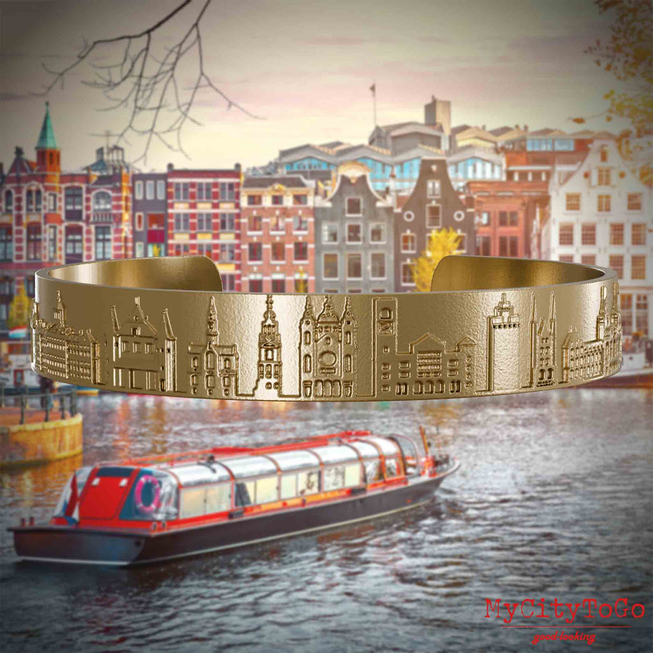 Armreif aus vergoldetem Edelstahl mit Reliefs bekannter Sehenswürdigkeiten der Stadt Amsterdam. Den Hintergrund bildet eine Ansicht der Stadt Amsterdam.