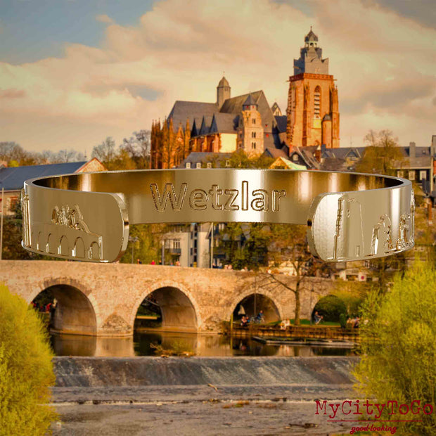Innenseite eines vergoldeten Armreifs mit Reliefs bekannter Sehenswürdigkeiten der Stadt Wetzlar und einer Gravur des Stadtnamens. Den Hintergrund bildet eine Ansicht der Stadt Wetzlar.
