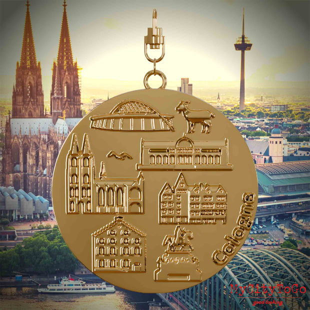 Halskette mit Drehwirbel und Vorderseite eines vergoldeten Schmuckanhängers, auf dem Reliefs bekannter Sehenswürdigkeiten der Stadt Koeln abgebildet sind. Den Hintergrund bildet eine Ansicht der Stadt Koeln.