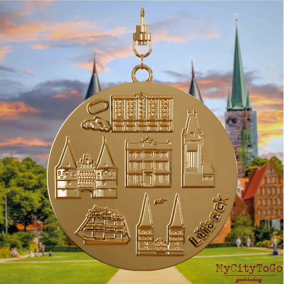 Halskette mit Drehwirbel und Rückseite eines vergoldeten Schmuckanhängers, auf dem Reliefs bekannter Sehenswürdigkeiten der Stadt Luebeck abgebildet sind. Den Hintergrund bildet eine Ansicht der Stadt Luebeck.
