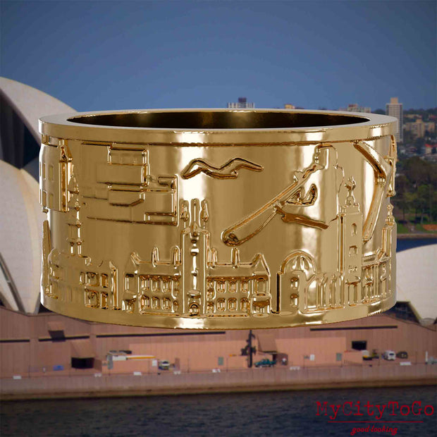 Vergoldeter Ring mit Reliefs bekannter Sehenswürdigkeiten der Stadt Sydney. Den Hintergrund bildet eine Ansicht der Stadt Sydney.