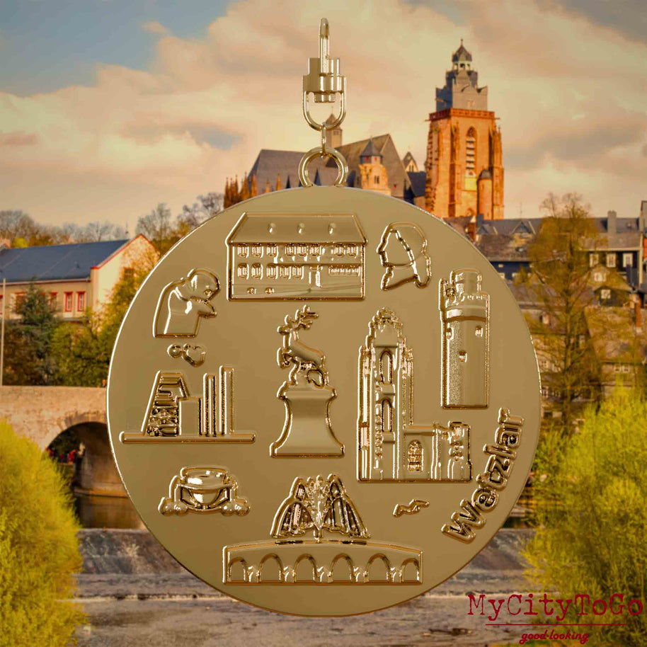 Halskette mit Drehwirbel und Rückseite eines vergoldeten Schmuckanhängers, auf dem Reliefs bekannter Sehenswürdigkeiten der Stadt Wetzlar abgebildet sind. Den Hintergrund bildet eine Ansicht der Stadt Wetzlar .
