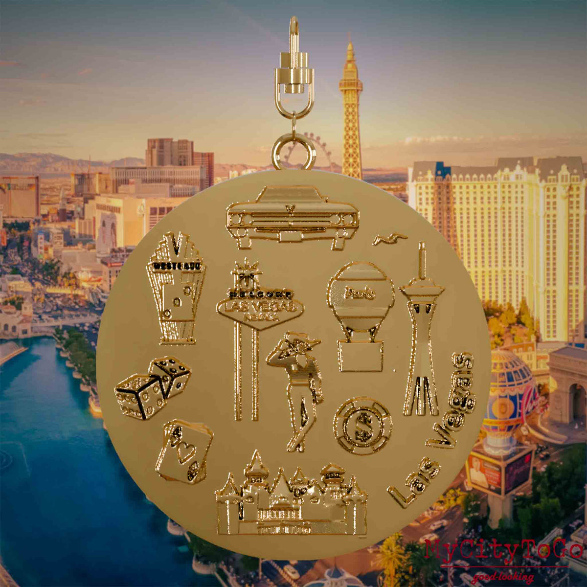 Halskette mit Drehwirbel und Rückseite eines vergoldeten Schmuckanhängers, auf dem Reliefs bekannter Sehenswürdigkeiten der Stadt Las Vegas abgebildet sind. Den Hintergrund bildet eine Ansicht der Stadt Las Vegas.