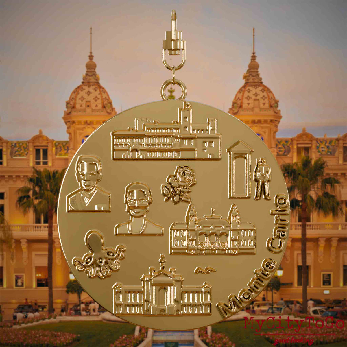 Halskette mit Drehwirbel und Rückseite eines vergoldeten Schmuckanhängers, auf dem Reliefs bekannter Sehenswürdigkeiten der Stadt Monte Carlo abgebildet sind. Den Hintergrund bildet eine Ansicht der Stadt Monte Carlo.
