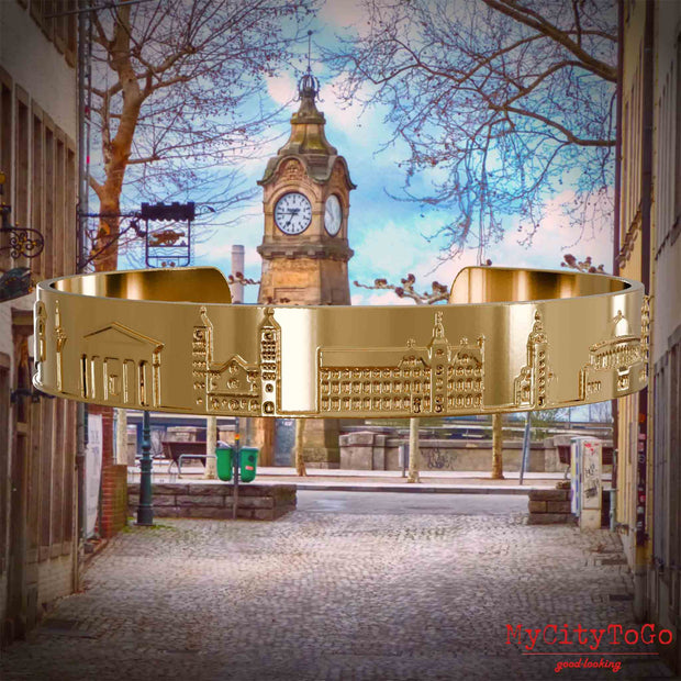 Vergoldeter Armreif mit Reliefs bekannter Sehenswürdigkeiten der Stadt Duesseldorf. Den Hintergrund bildet eine Ansicht der Stadt Duesseldorf.