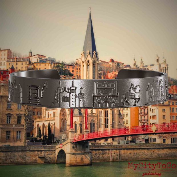 Armreif aus Titan mit Reliefs bekannter Sehenswürdigkeiten der Stadt Lyon. Den Hintergrund bildet eine Ansicht der Stadt Lyon.