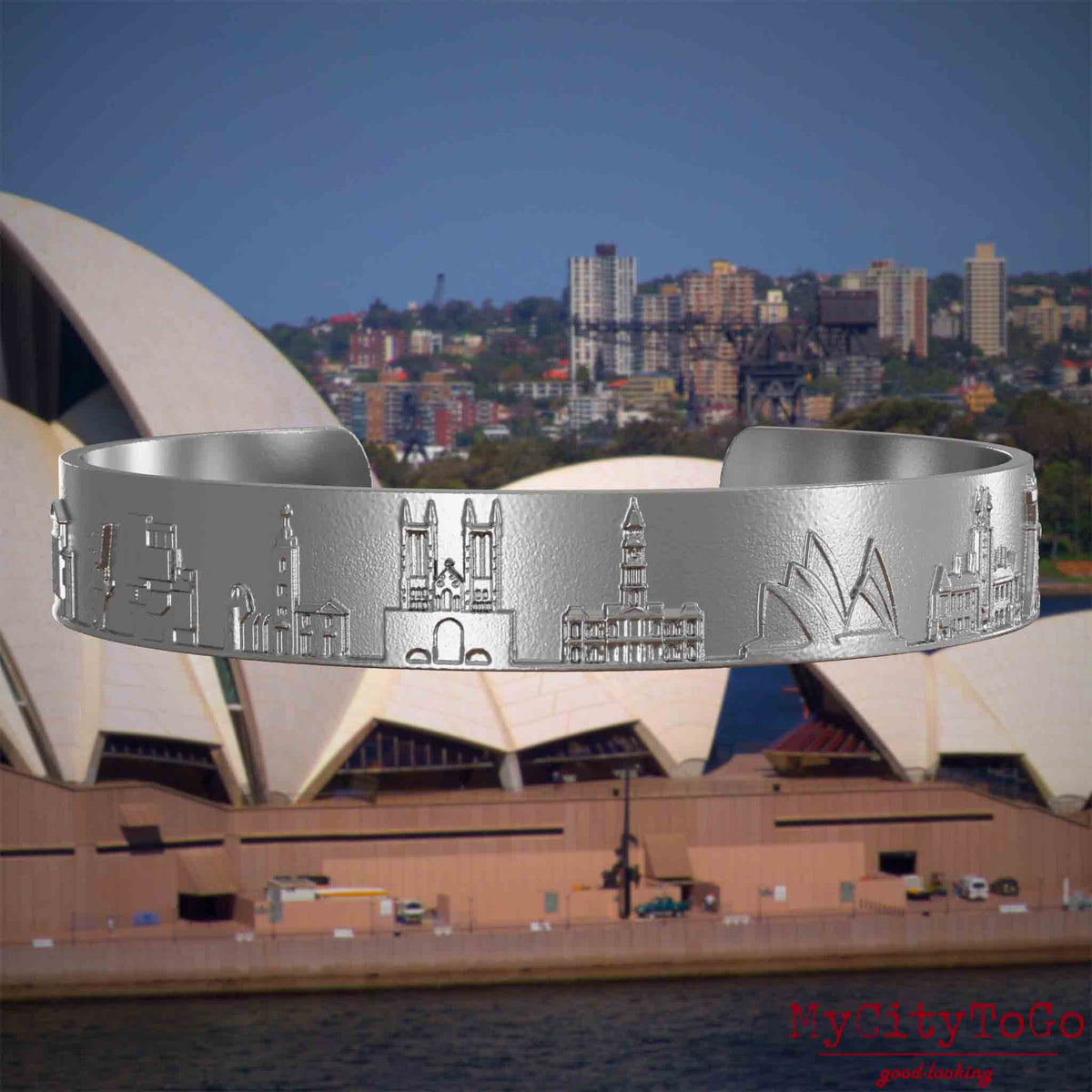 Armreif aus Edelstahl mit Reliefs bekannter Sehenswürdigkeiten der Stadt Sydney. Den Hintergrund bildet eine Ansicht der Stadt Sydney.