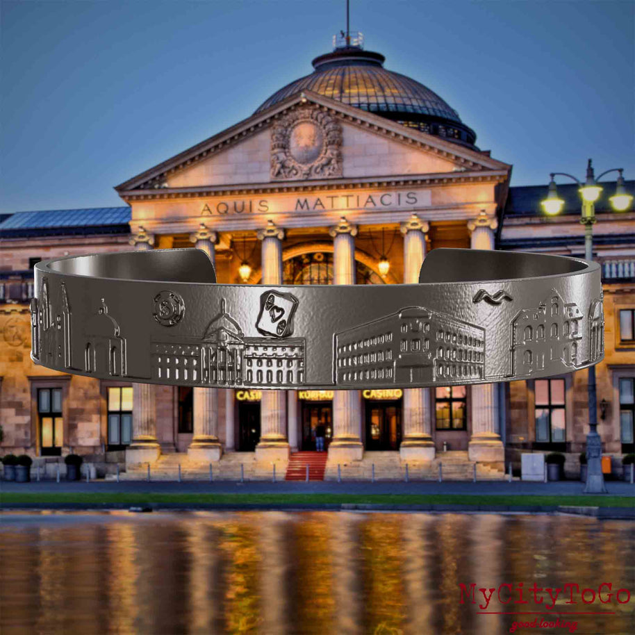 Armreif aus Titan mit Reliefs bekannter Sehenswürdigkeiten der Stadt Wiesbaden. Den Hintergrund bildet eine Ansicht der Stadt Wiesbaden.