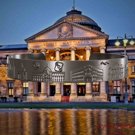 Armreif aus Titan mit Reliefs bekannter Sehenswürdigkeiten der Stadt Wiesbaden. Den Hintergrund bildet eine Ansicht der Stadt Wiesbaden.