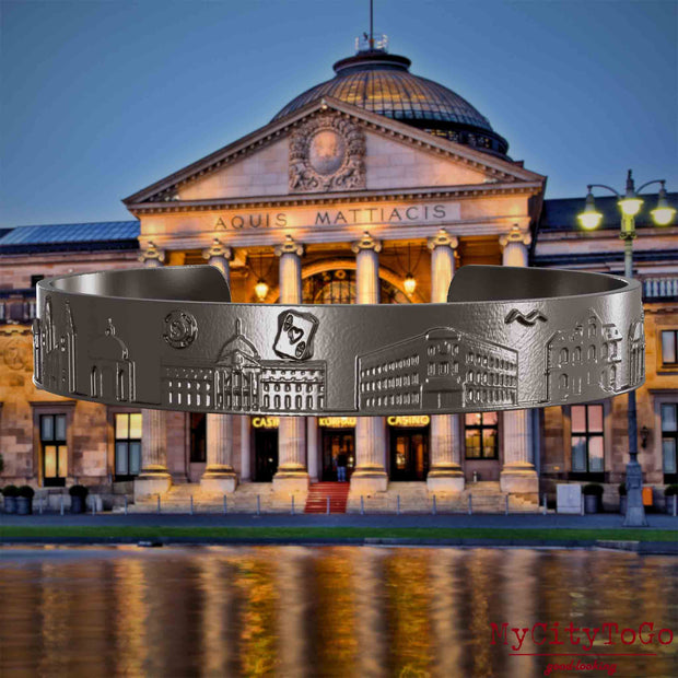 Armreif aus Titan mit Reliefs bekannter Sehenswürdigkeiten der Stadt Wiesbaden. Den Hintergrund bildet eine Ansicht der Stadt Wiesbaden.