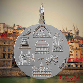 Halskette mit Drehwirbel und Rückseite eines silbernen Schmuckanhängers, auf dem Reliefs bekannter Sehenswürdigkeiten der Stadt Lyon abgebildet sind. Den Hintergrund bildet eine Ansicht der Stadt Lyon.
