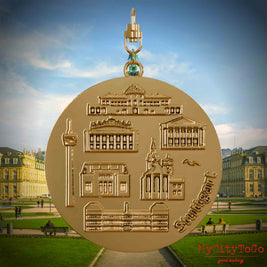 Halskette mit Drehwirbel und Vorderseite eines vergoldeten Schmuckanhängers, auf dem Reliefs bekannter Sehenswürdigkeiten der Stadt Stuttgart abgebildet sind. Den Hintergrund bildet eine Ansicht der Stadt Stuttgart.
