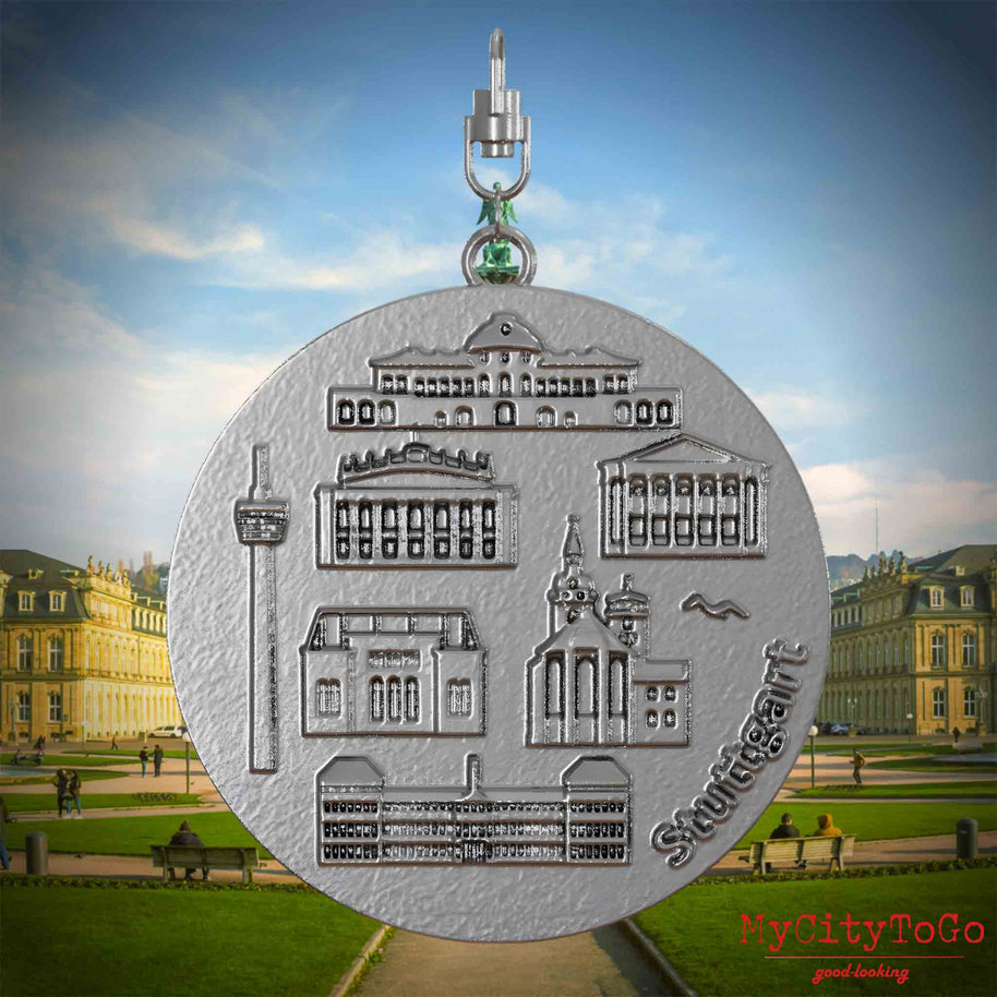 Halskette mit Drehwirbel und Vorderseite eines Schmuckanhängers aus Edelstahl, auf dem Reliefs bekannter Sehenswürdigkeiten der Stadt Stuttgart abgebildet sind. Den Hintergrund bildet eine Ansicht der Stadt Stuttgart.
