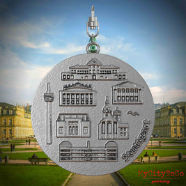 Halskette mit Drehwirbel und Vorderseite eines Schmuckanhängers aus Edelstahl, auf dem Reliefs bekannter Sehenswürdigkeiten der Stadt Stuttgart abgebildet sind. Den Hintergrund bildet eine Ansicht der Stadt Stuttgart.
